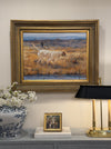 At Point framed sporting oil painting hung above a console styled with a brass lamp, blue-and-white jar, white flowers, and books
