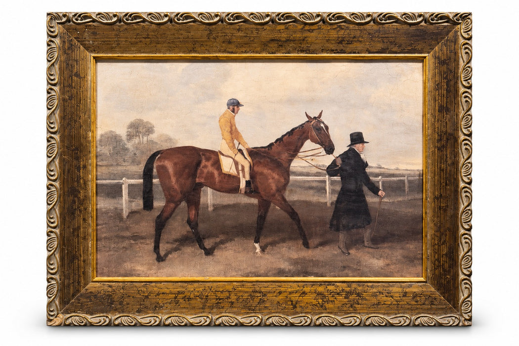 The Paddock antique framed equestrian scene of a jockey in yellow silks on a bay horse led along a rail by a man in a top hat, in a distressed bronze-gold scroll-edge frame